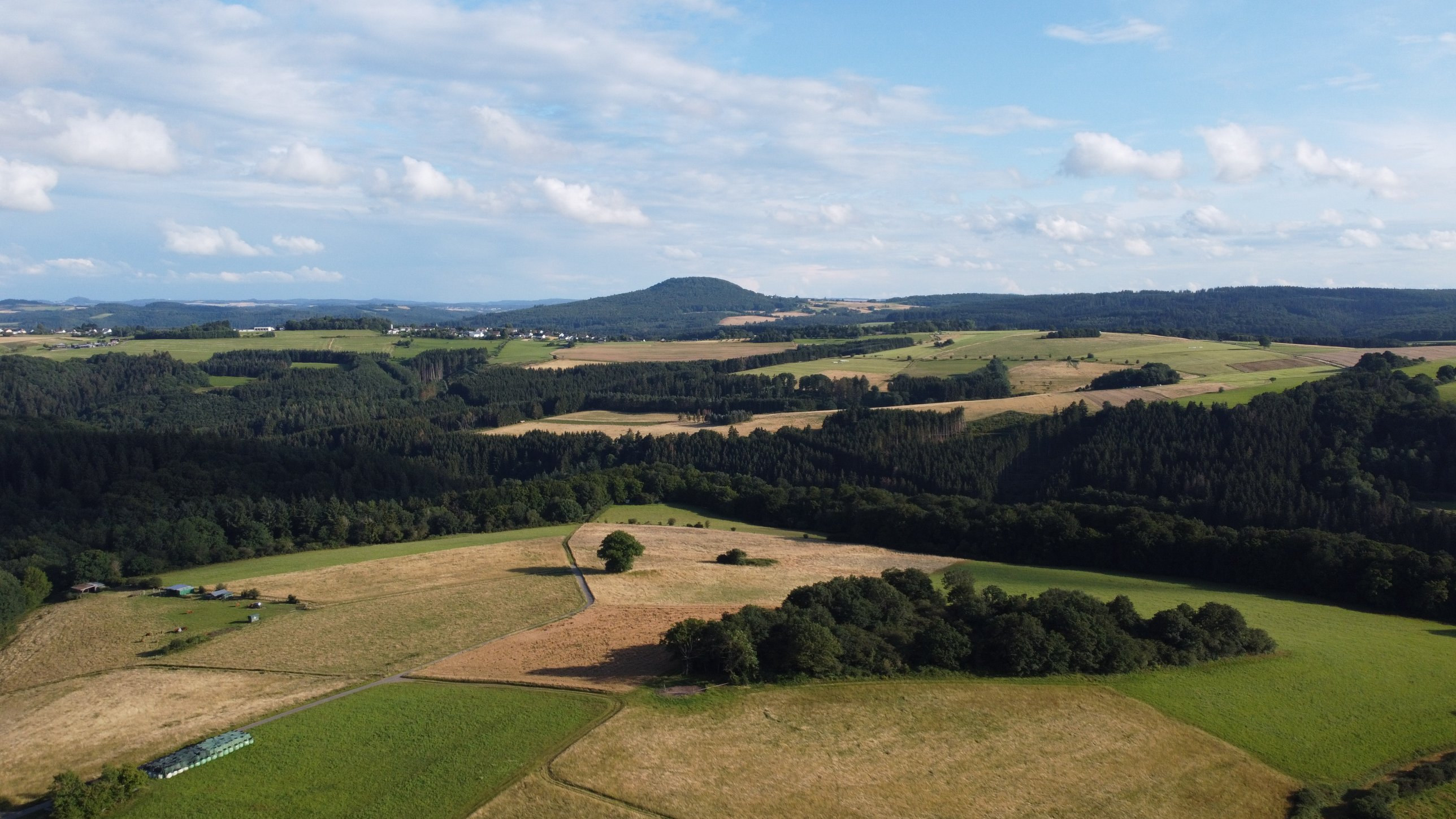 Drohnenaufnahme der Eifel bei Hümmel-Marthel im Sommer: Felder, Wälder und ein Bergkegel am Horizont
